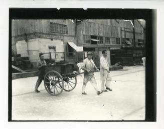 Three dockyard workers pulling a cart