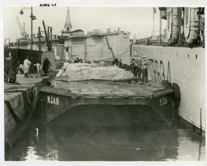 Dockyard workers of the R.N.A.D. (Royal Naval Armaments Depot) load "HMS ST AUSTELL BAY" (F634) with armaments