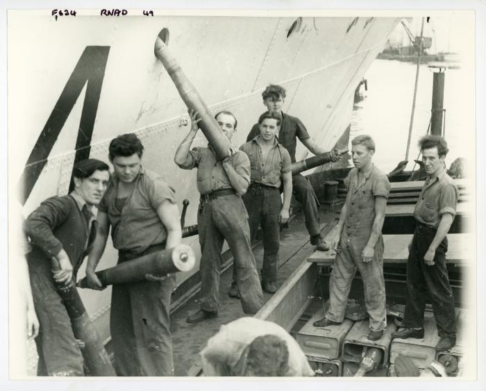 Dockyard workers of the R.N.A.D. (Royal Naval Armaments Depot) load "HMS ST AUSTELL BAY" (F634) with armaments