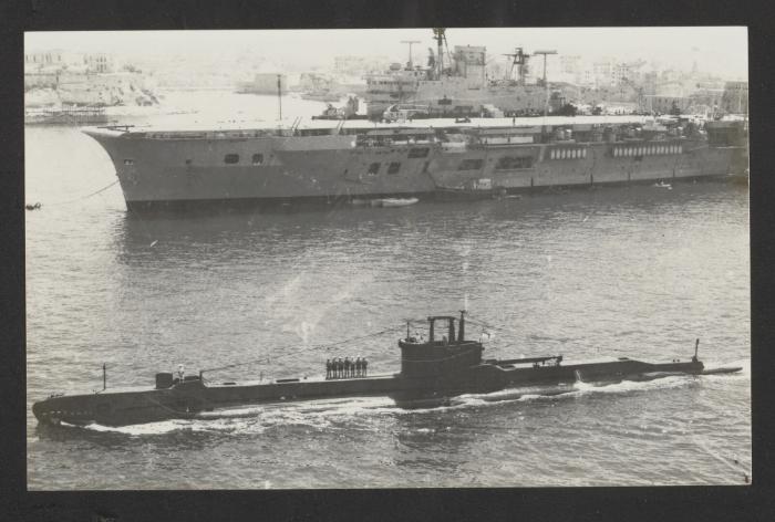 British S-class submarine HMS Sentinel (P256) with Audacious-class aircraft carrier HMS Eagle (R05) in the background, pre-refit and with a Westland Whirlwind helicopter aboard, at Grand Harbour, Malta