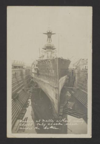 A British surface warship, possibly an Iron Duke-class battleship, at the Malta Drydock. Recto caption reads, "Docked at Malta without using shores. Only chocks used under the bottom".