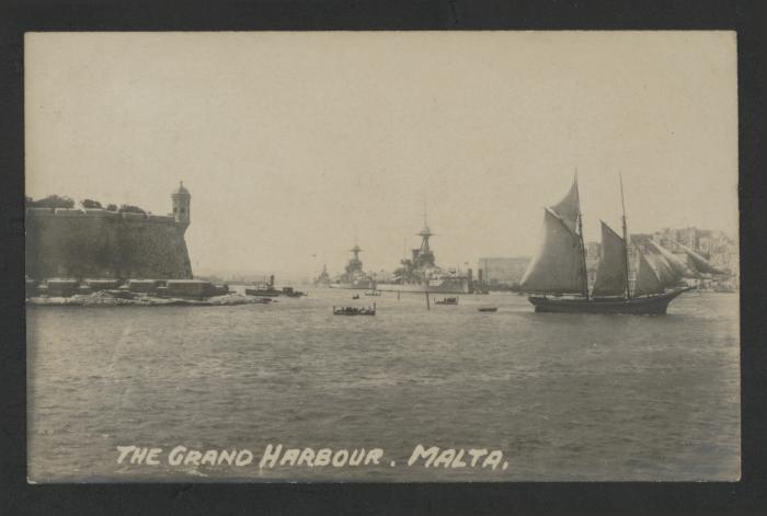 View of the Grand Harbour, Malta, with a sailing vessel and Maltese dgħajsa boats in the foreground, and several British capital ships in the background